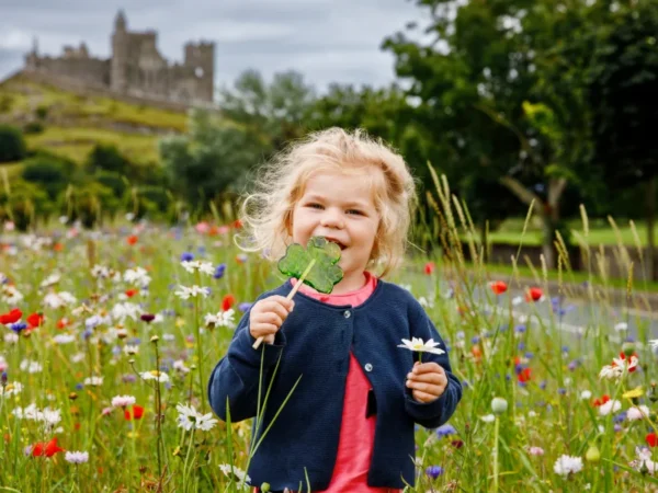 Cute girl with Irish cloverleaf lollipop with Rock of Cashel castle on background, family travel tips in our blog © Adobe Stock