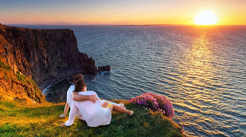 Couple in hug watching sunset on the edge of the cliff. Romantic getaways in Ireland.