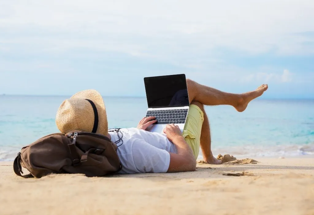 Man relaxing on the beach browsing on his laptop - Why Book Direct wth Trident Holiday Homes